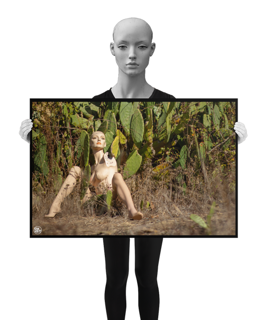 un4rt - almost human gallery poster mockup picture with a mannequin sitting outdoor in in front of a huge cactus. dried gras on the ground. the poster is held by a mannequin.
