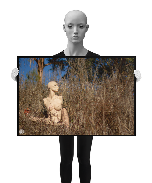 un4rt - almost human gallery poster mockup picture with a mannequin sitting outdoor in between very high and dried brown gras. some trees and blue sky in the background. the poster is held by a mannequin.