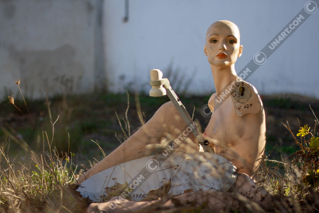 un4rt - almost human gallery poster mockup picture with a mannequin sitting outdoor next to an old satelite dish. white stonewall in the background.