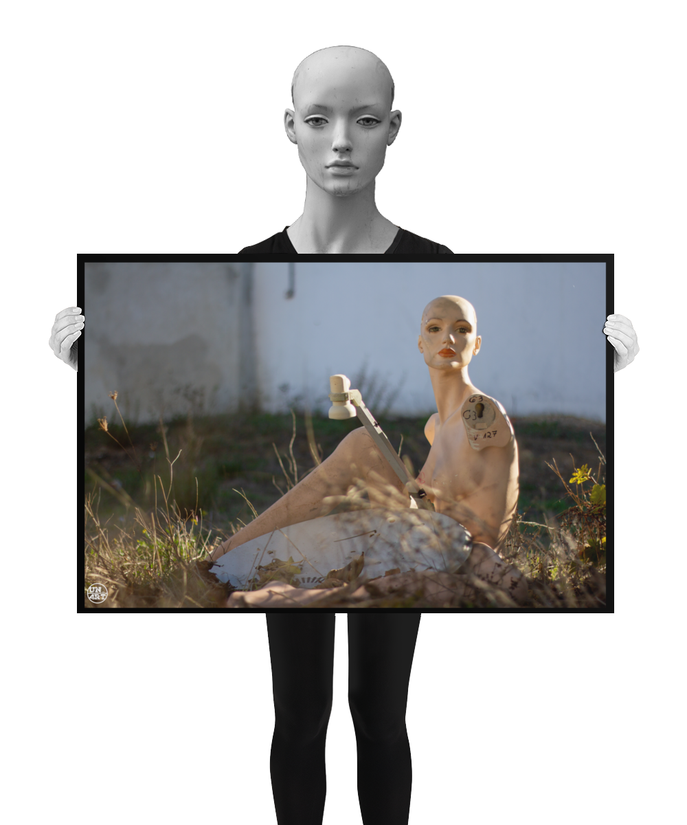 un4rt - almost human gallery poster mockup picture with a mannequin sitting outdoor next to an old satelite dish. white stonewall in the background. the poster is held by a mannequin.