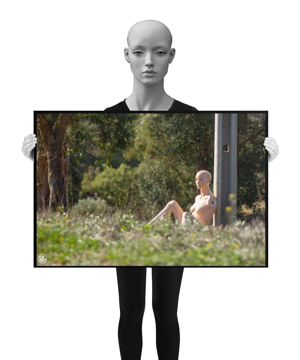 un4rt - almost human gallery poster mockup picture with a mannequin sitting outdoor during summer. the model leans against a concrete pole. the poster is held by a mannequin.