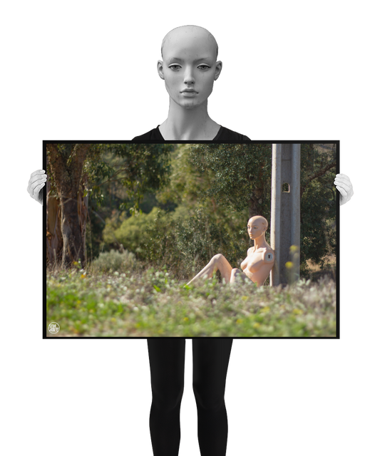 un4rt - almost human gallery poster mockup picture with a mannequin sitting outdoor during summer. the model leans against a concrete pole. the poster is held by a mannequin.