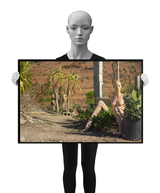un4rt - almost human gallery poster mockup picture with a mannequin sitting outdoor in between some plants. the poster is held by a mannequin.