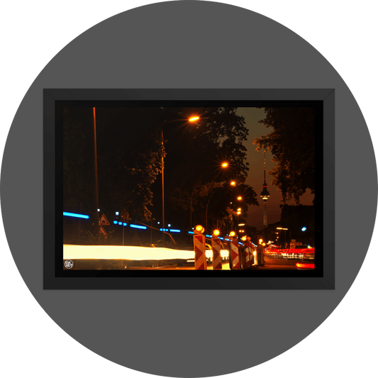 un4rt - the photographie shows a street in berlin. the street is called "puschkinallee" and the view goes along a construction site. at the end of the street berlin´s television tower is clearly visible. time lapse. golden hour. trees and city lights.