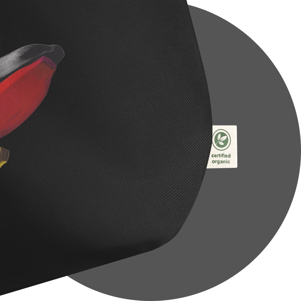 un4rt - the image shows details of a black cotton tote bag with a print on it. the print is only partially visible and shows the endings of three bananas, colored in black, red and yellow. a white label with a green print is attached to the tote bag. the print on the label says: "certified organic".