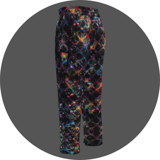 UN4RT cosmic grid all-over-print jogging pants back left view – dark sweatpants with three-dimensional black sphere and bubble cluster pattern, iridescent neon rainbow glow in pink, blue, orange and teal between forms, small UN4RT logo at lower leg, elasticated waistband, straight leg cut.