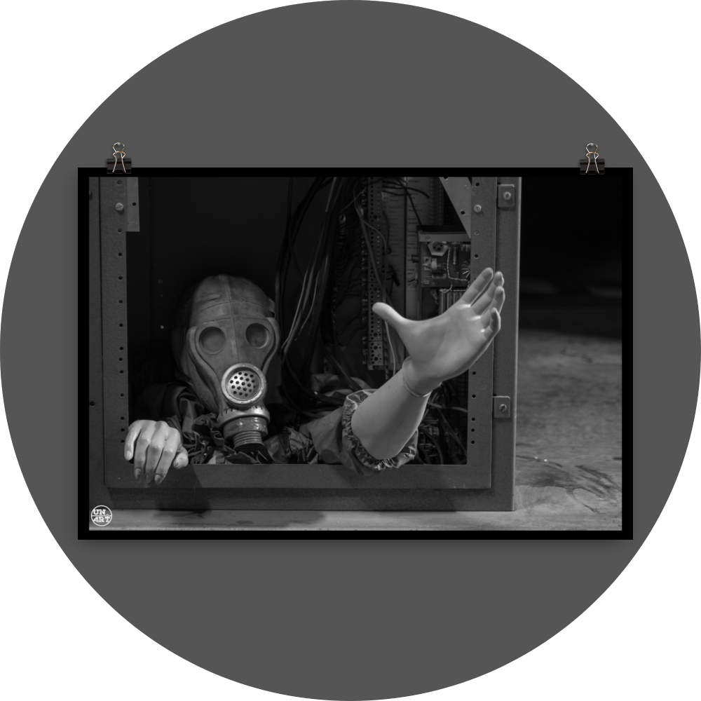 un4rt - black and white photographie of a mannequin wearing a gas mask. the mannequin stretches out one arm and reaches for help. the body is stuck inside a box with wires and electronic parts.