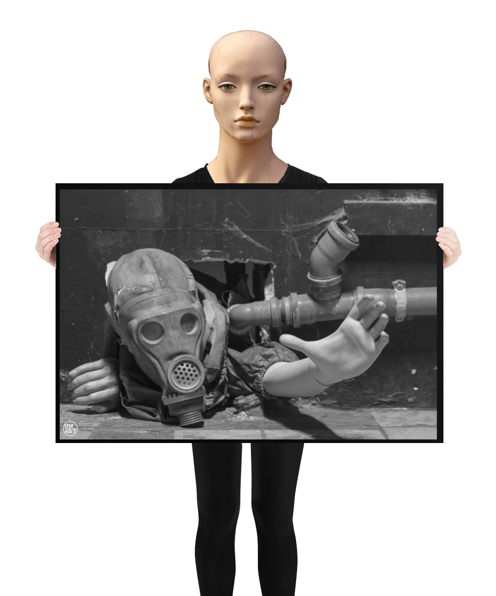 un4rt - a poster. black and white photographie of a mannequin wearing a gas mask. the mannequin stretches out one arm and reaches for help. the body is stuck inside a small hole in a wall. unused blackwater pipes next to the mannequin. a mannequin is holding the poster.