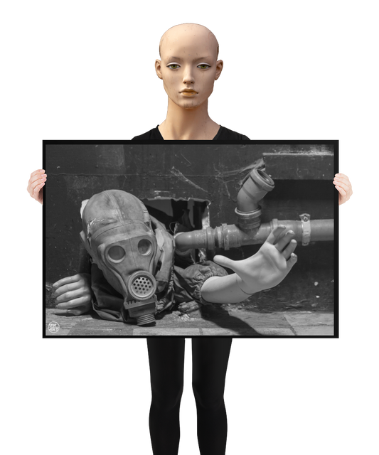 un4rt - a poster. black and white photographie of a mannequin wearing a gas mask. the mannequin stretches out one arm and reaches for help. the body is stuck inside a small hole in a wall. unused blackwater pipes next to the mannequin. a mannequin is holding the poster.