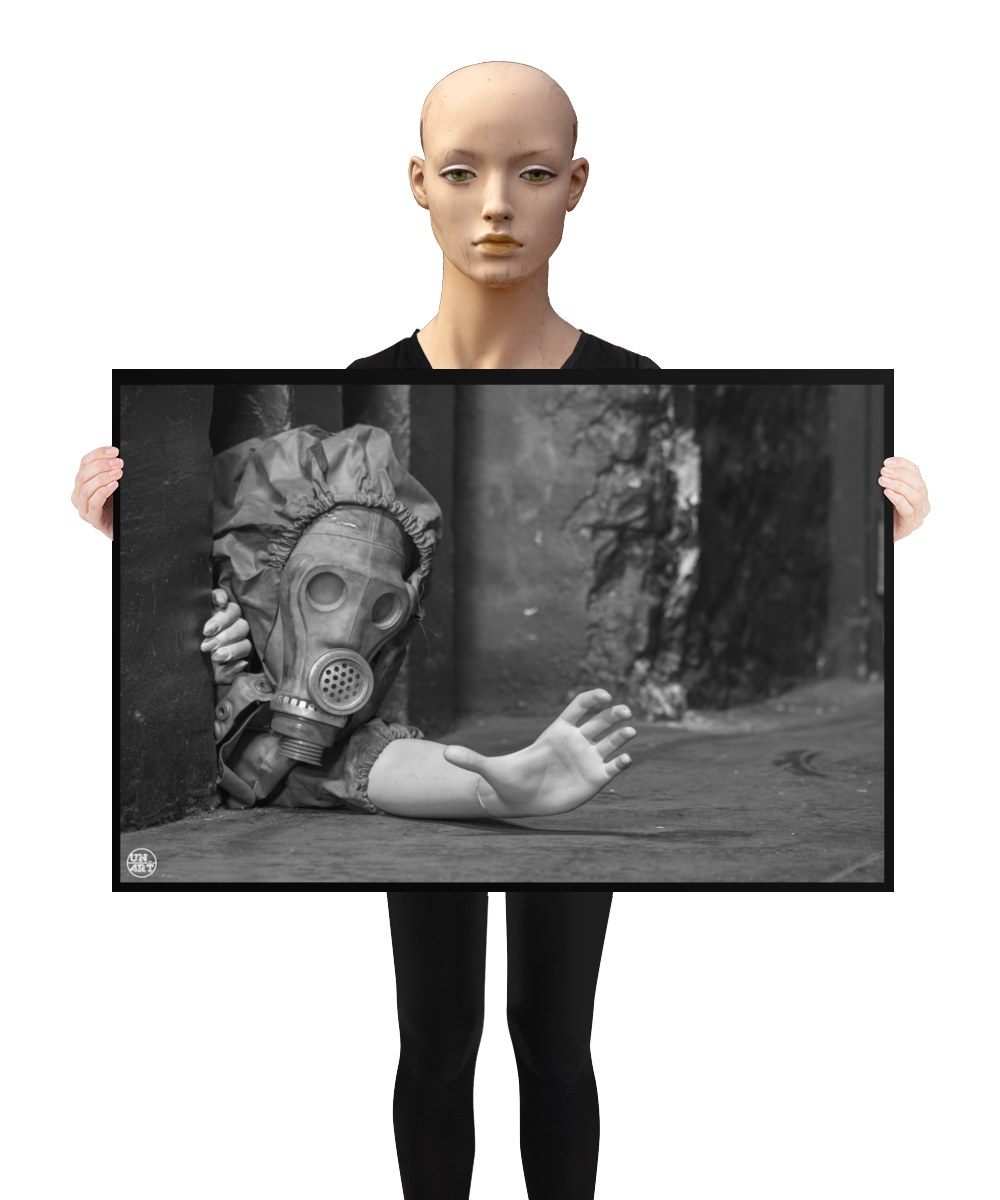 un4rt - a poster. black and white photographie of a mannequin wearing a gas mask. the mannequin stretches out one arm and reaches for help. the mannequin is crawling out of a tiny hole in the wall, directly on the floor. a mannequin is holding the poster.
