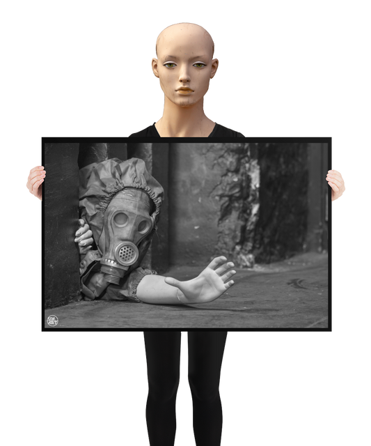 un4rt - a poster. black and white photographie of a mannequin wearing a gas mask. the mannequin stretches out one arm and reaches for help. the mannequin is crawling out of a tiny hole in the wall, directly on the floor. a mannequin is holding the poster.