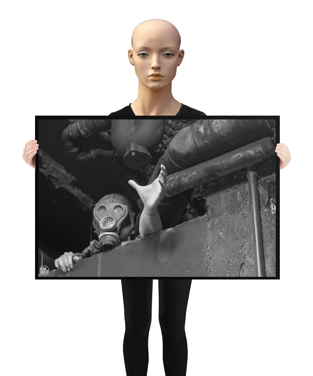 un4rt - a poster. black and white photographie of a mannequin wearing a gas mask. the mannequin stretches out one arm and reaches for help. the mannequin is stuck between a wall and a ceiling inside a cellar. waste water pipes above the mannequin. a mannequin is holding the poster.