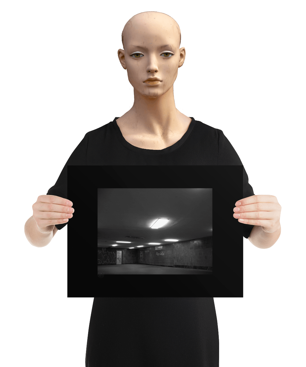 un4rt - a black and white photographie of a former underground trespas that once was part of the train station "alexanderplatz in berlin. the image shows a corner with a closed door. graffities on the wall. one lamp on the ceiling is broken. he image is held by a mannequin.