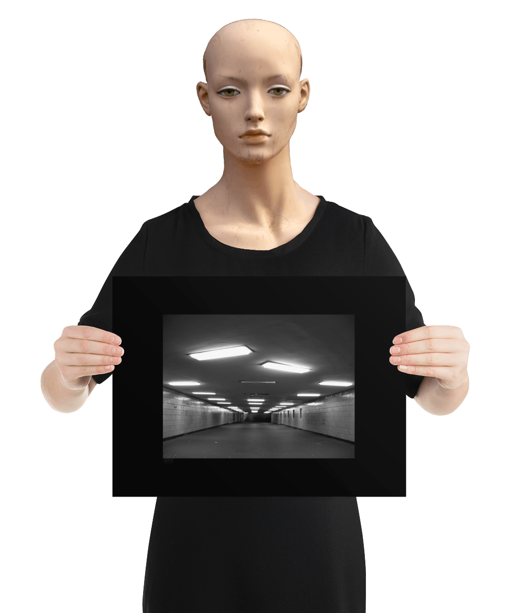 un4rt - a black and white photographie of a former underground trespas that once was part of the train station "alexanderplatz in berlin. the walls are tiled. some graffities on the walls and placeholders for advertising posters. trash on the floor. some lights n the ceiling don´t work. the image is held by a mannequin.