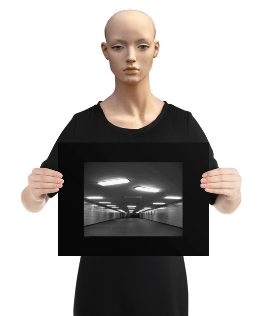 un4rt - a black and white photographie of a former underground trespas that once was part of the train station "alexanderplatz in berlin. the walls are tiled. some graffities on the walls and placeholders for advertising posters. trash on the floor. some lights n the ceiling don´t work. the image is held by a mannequin.