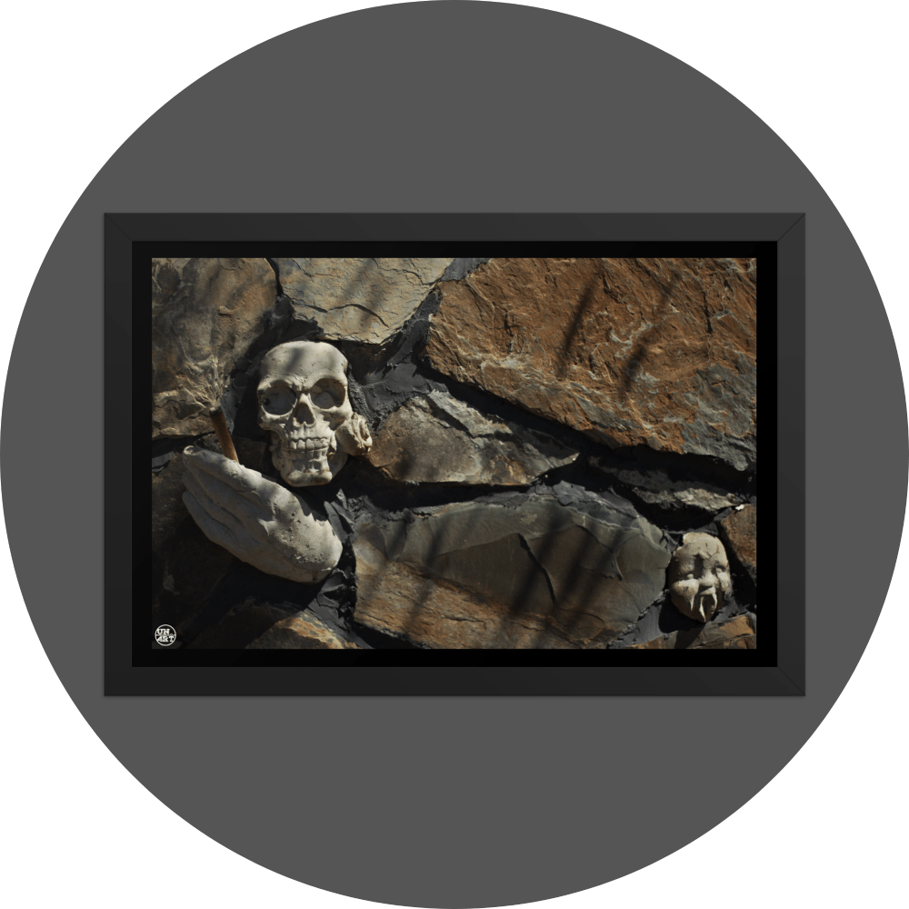 un4rt - the photographie shows some stones that are art of a bigger stone wall. a plaster skull with a rose in its mouth, a plaster hand with a joint and a baby face with plaster vampire teeth decorate the wall.