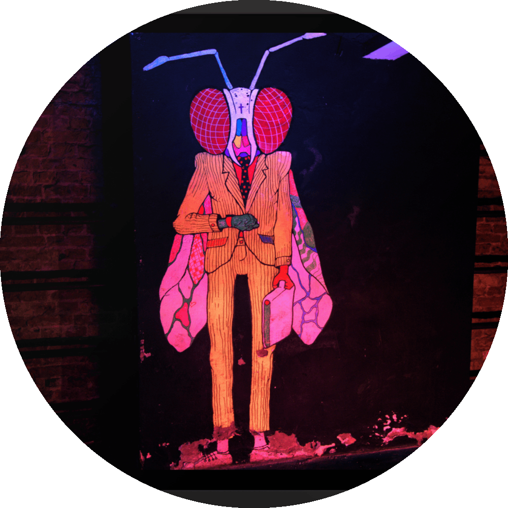 un4rt - the photographie shows a mural of a humanoid insect in a suit with a briefcase on a black wall. the creature is looking at a watch on his wrist. on both side of the black wall there re brick walls with fixed steel pipes. the creature is colorful with a yellow suit, red eyes colored wings and a white head.