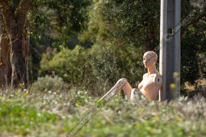 un4rt - almost human gallery poster mockup picture with a mannequin sitting outdoor during summer. the model leans against a concrete pole. 
