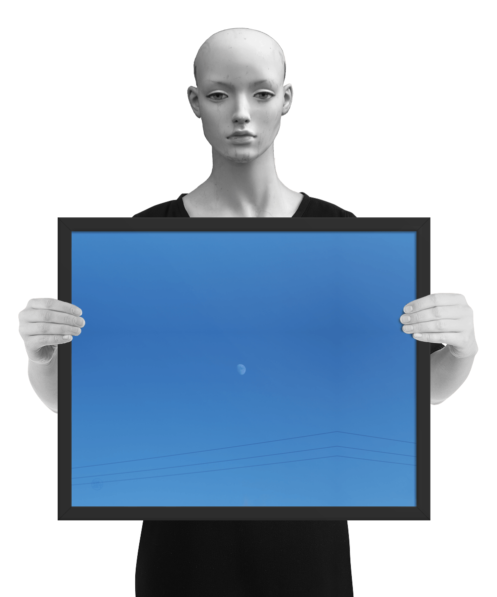 un4rt - the photographie shows a completely blue sky with a small moon in the center. some power lines cross the image on the bottom. the image is framed and presented by a mannequin in black and white.