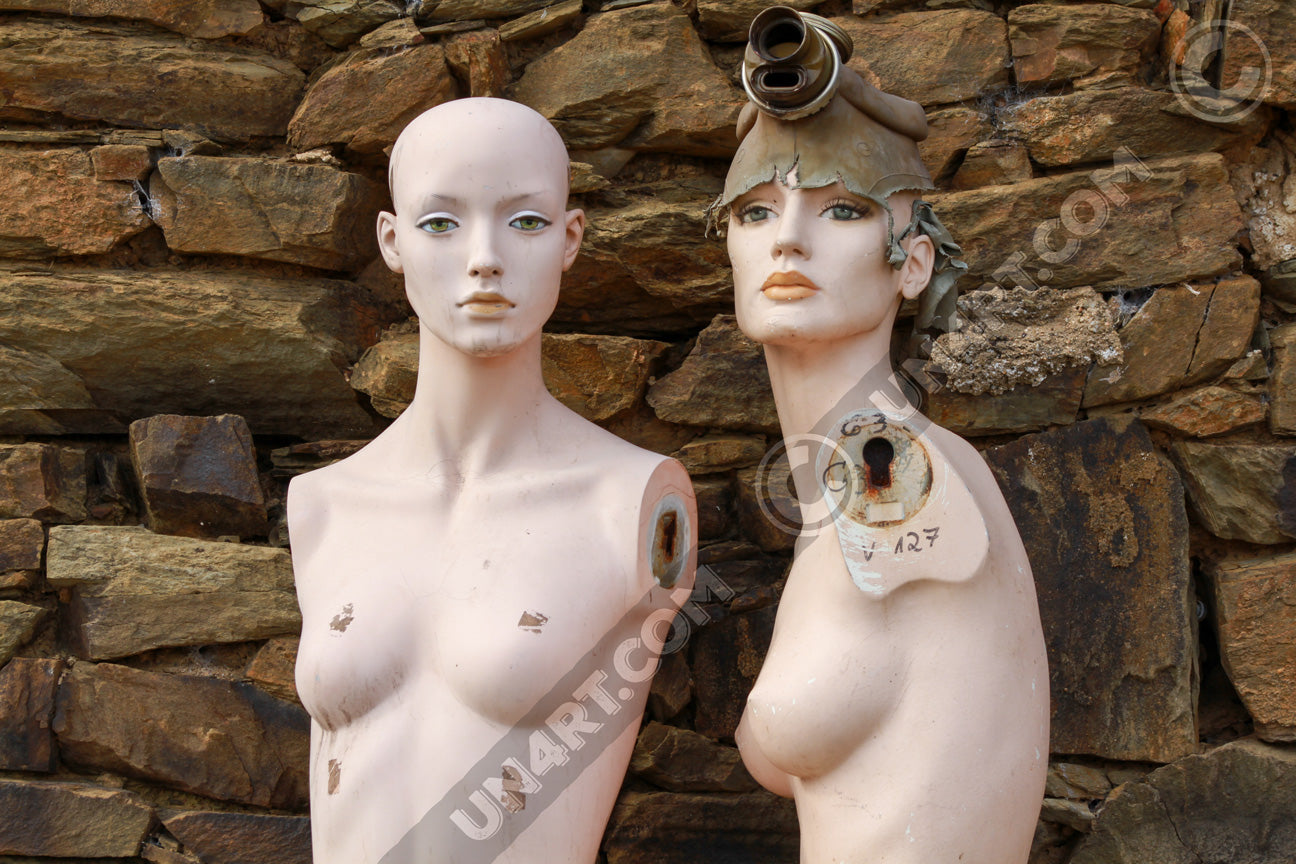 un4rt photographie of two mannequins in front of an old stonewall. both mannequins have no arms. one mannequin is wearing a gas mask. both mannequins look to the camera.