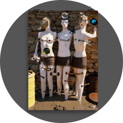 un4rt - combination of photographie and ai-art. three mannequins are chained together. they are standing in mud, in front of an old stone wall. one of the mannequins is looking into the camera, the others are wearing a gas mask and face away from the camera. each mannequin is in a relationship with a glas orb.