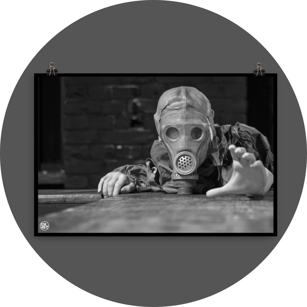 un4rt - black and white photographie of a mannequin wearing a gas mask. the mannequin stretches out one arm and reaches for help. the mannequin lies on a wooden planket, but the body is not visible. direct front view. black brick wall in the background.