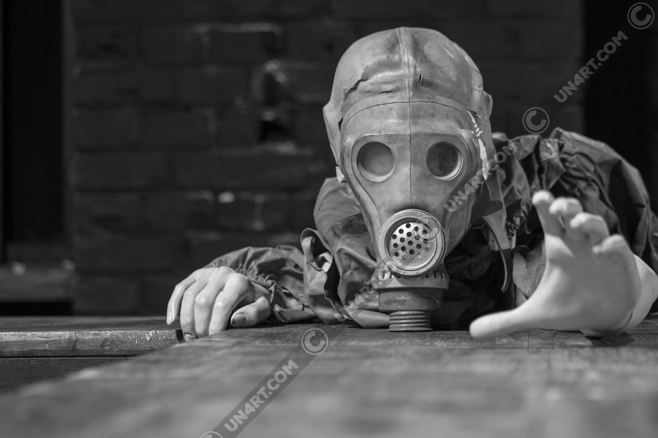 un4rt - black and white photographie of a mannequin wearing a gas mask. the mannequin stretches out one arm and reaches for help. the mannequin lies on a wooden planket, but the body is not visible. direct front view. black brick wall in the background.
