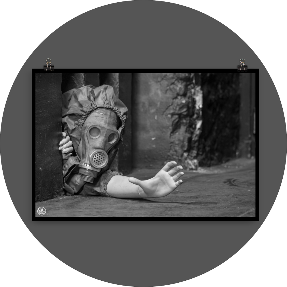un4rt - black and white photographie of a mannequin wearing a gas mask. the mannequin stretches out one arm and reaches for help. the mannequin is crawling out of a tiny hole in the wall, directly on the floor.