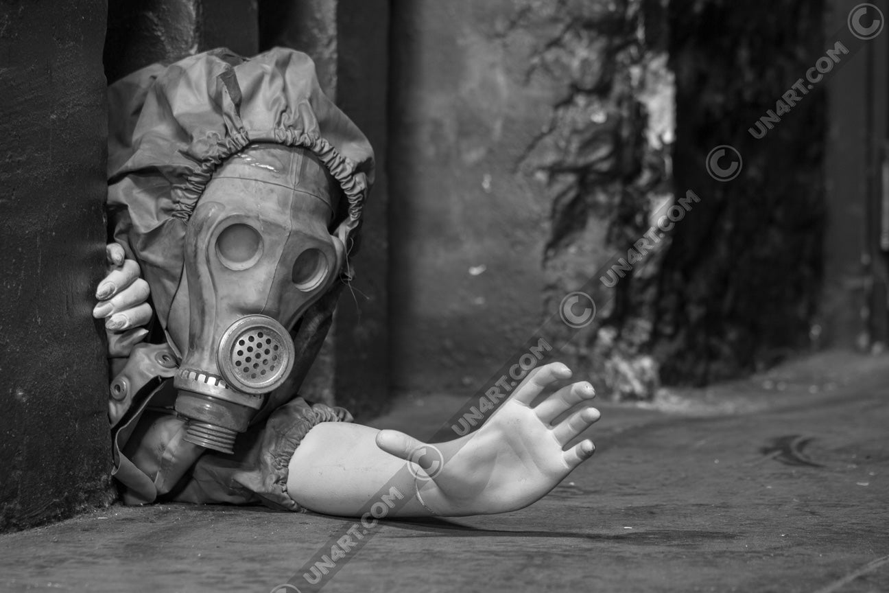 un4rt - black and white photographie of a mannequin wearing a gas mask. the mannequin stretches out one arm and reaches for help. the mannequin is crawling out of a tiny hole in the wall, directly on the floor.