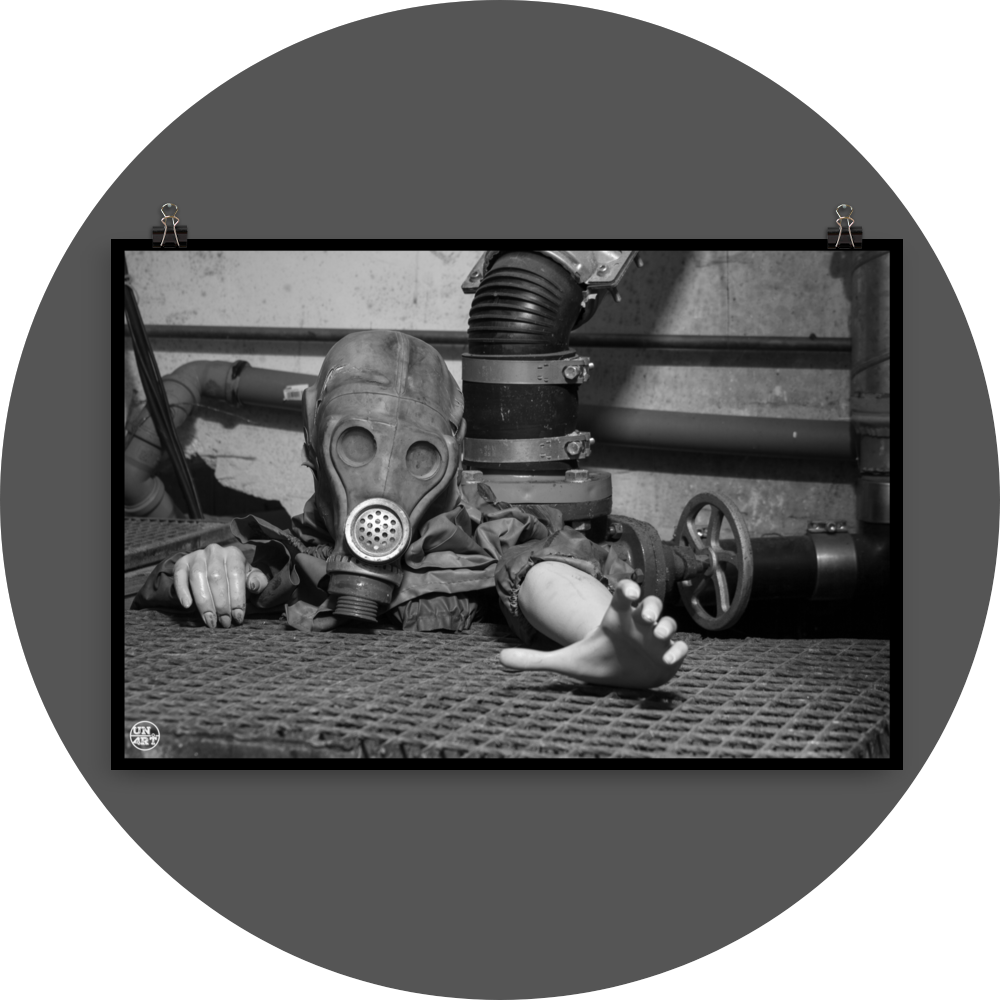 un4rt - black and white photographie of a mannequin wearing a gas mask. the mannequin stretches out one arm and reaches for help. the mannequin is crawling out of a hole in the ground. grif floor ground. pipes and a shut-off valve next to the mannequin.