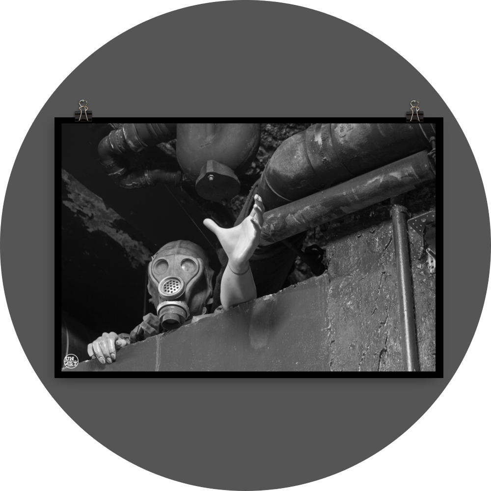 un4rt - black and white photographie of a mannequin wearing a gas mask. the mannequin stretches out one arm and reaches for help. the mannequin is stuck between a wall and a ceiling inside a cellar. waste water pipes above the mannequin.