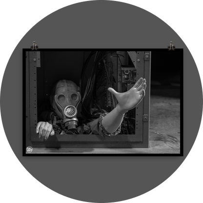un4rt - black and white photographie of a mannequin wearing a gas mask. the mannequin stretches out one arm and reaches for help. the body is stuck inside a box with wires and electronic parts. 