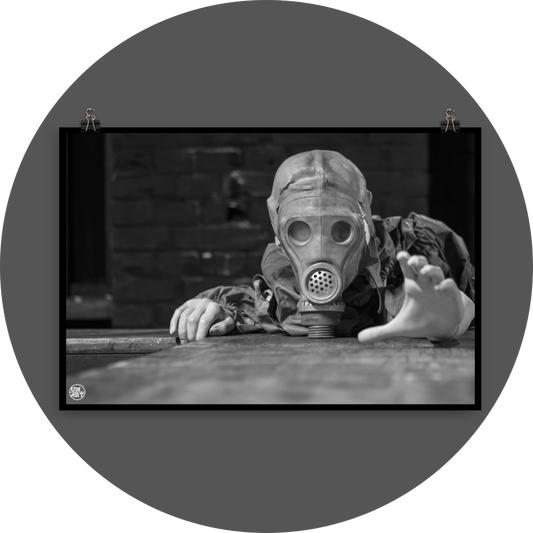 un4rt - black and white photographie of a mannequin wearing a gas mask. the mannequin stretches out one arm and reaches for help. the mannequin lies on a wooden planket, but the body is not visible. direct front view. black brick wall in the background.