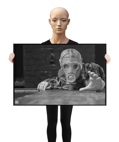un4rt - a poster. black and white photographie of a mannequin wearing a gas mask. the mannequin stretches out one arm and reaches for help. the mannequin lies on a wooden planket, but the body is not visible. direct front view. black brick wall in the background. a mannequin s holding the poster.