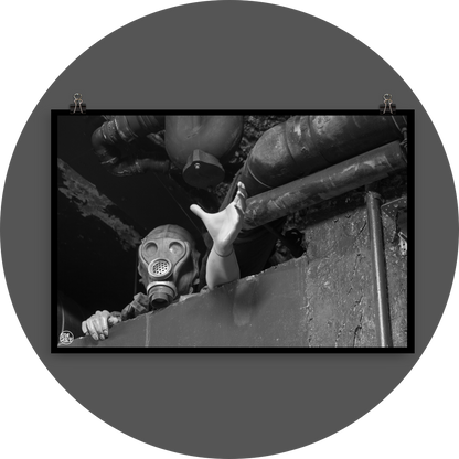 un4rt - black and white photographie of a mannequin wearing a gas mask. the mannequin stretches out one arm and reaches for help. the mannequin is stuck between a wall and a ceiling inside a cellar. waste water pipes above the mannequin.