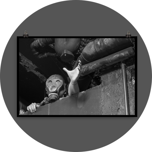 un4rt - black and white photographie of a mannequin wearing a gas mask. the mannequin stretches out one arm and reaches for help. the mannequin is stuck between a wall and a ceiling inside a cellar. waste water pipes above the mannequin.