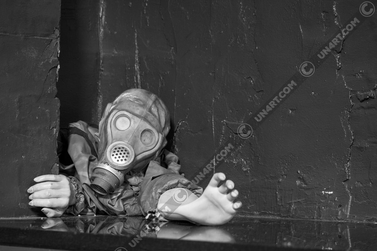 un4rt - black and white photographie of a mannequin wearing a gas mask and forcing its way through a tiny gap between two walls. the mannequing stretches out one arm and reaches for help. 