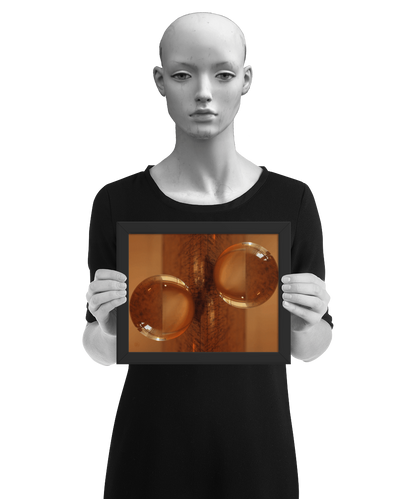 un4rt - the photographie is doubled and then mirrored. both photographies together create the final image. the photographie shows a glass ball on a wooden board. the wooden board is reflecting inside the glasball. the colors range from light brown to orange. the image is framed and presented by a mannequin in black and white.