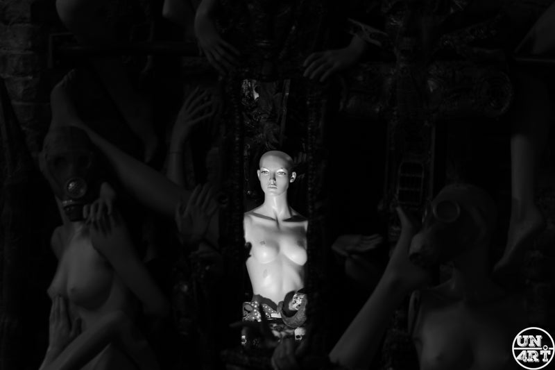 UN4RT imaginarium – illuminated bald female mannequin torso centred in a dark crowd of shadowy figures, black and white fine art photography.