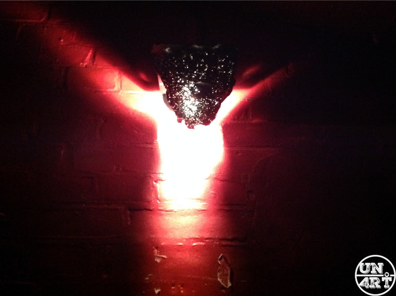 UN4RT imaginarium – reflecting light formig a glowing body below a coverd white light on a dark brick wall, dark symbolic art.
