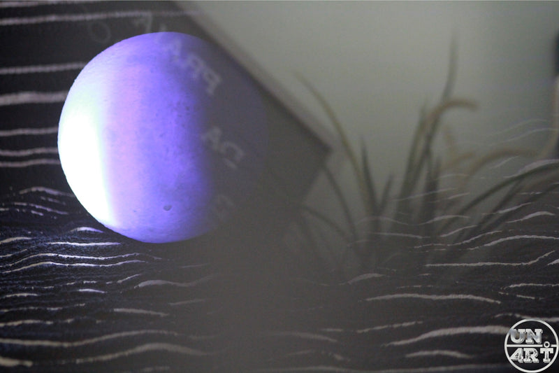 UN4RT imaginarium – glowing purple sphere floating above hand-drawn wave lines beside a shadow of tall grass, minimalist surreal art photography.