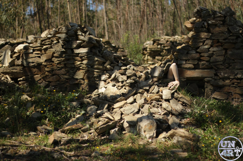 UN4RT imaginarium – bare human arm emerging from collapsed dry stone wall ruins in a sunlit woodland clearing, dark surreal fine art photography.