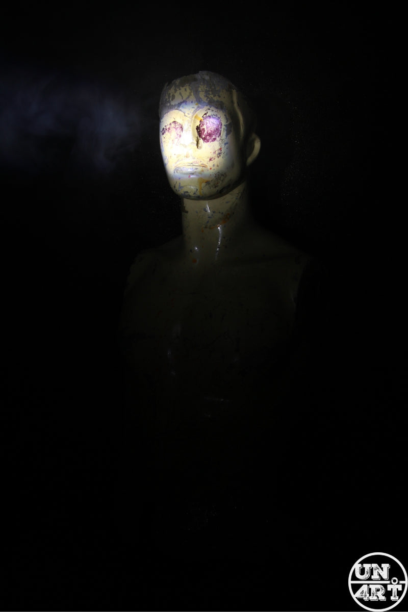 UN4RT imaginarium – decayed humanoid bust with hollow purple eye sockets emerging from darkness under a single spotlight, dark horror sculpture photography.