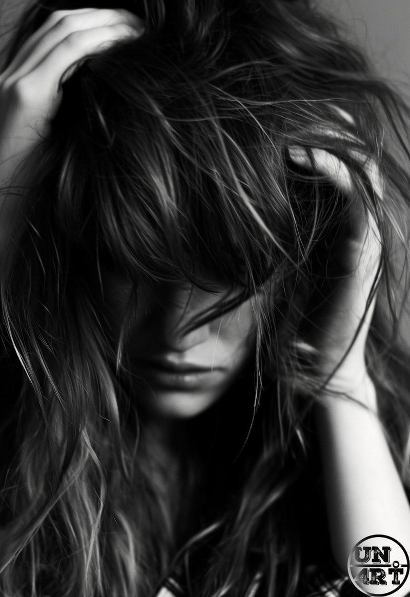 UN4RT imaginarium – close-up black and white portrait of a woman with wild tousled long dark hair obscuring her face as both hands rake through it against a soft grey background, dark emotive fashion editorial photography.