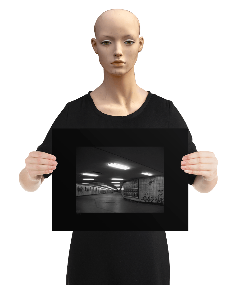 un4rt - a black and white photographie of a former underground trespas that once was part of the train station "alexanderplatz in berlin. advertisings and graffities on the wall. the image is held by a mannequin.