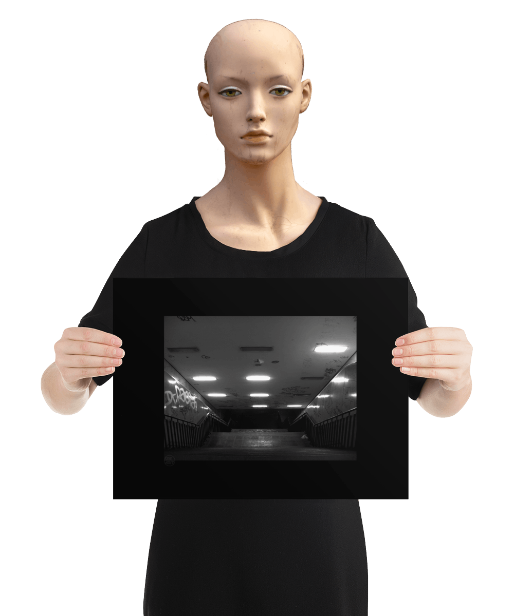 un4rt - a black and white photographie of a former underground trespas that once was part of the train station "alexanderplatz in berlin. a stairway that is leading down. graffities on the ceiling and the wall. the image is held by a mannequin.