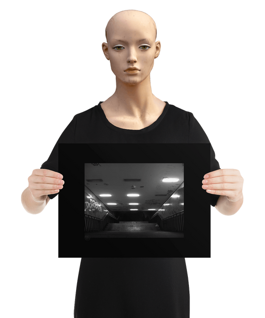 un4rt - a black and white photographie of a former underground trespas that once was part of the train station "alexanderplatz in berlin. a stairway that is leading down. graffities on the ceiling and the wall. the image is held by a mannequin.