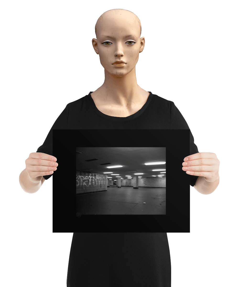 un4rt - a black and white photographie of a former underground trespas that once was part of the train station "alexanderplatz in berlin. graffities on the wall, trash on the ground. some lights on the ceiling don´t work. a stairway at the end of the trespas. the image is held by a mannequin.