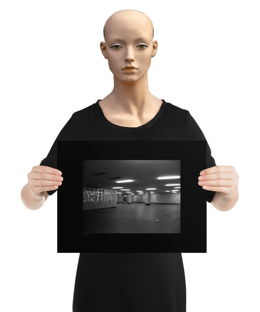 un4rt - a black and white photographie of a former underground trespas that once was part of the train station "alexanderplatz in berlin. graffities on the wall, trash on the ground. some lights on the ceiling don´t work. a stairway at the end of the trespas. the image is held by a mannequin.