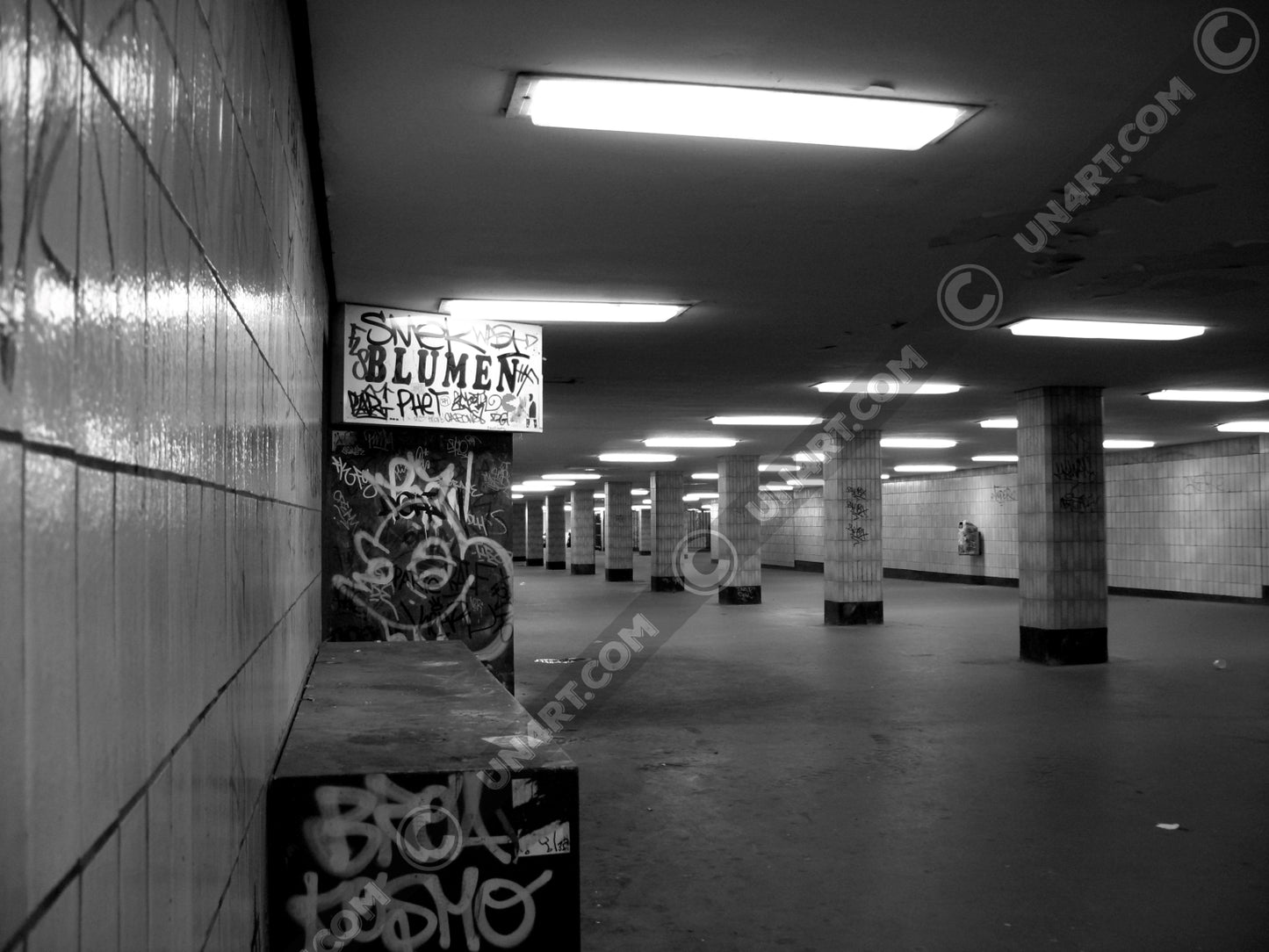 un4rt - a black and white photographie of a former underground trespas that once was part of the train station "alexanderplatz in berlin. tiled square columns support the ceiling. the left wall also has a porch of an old flower shop. the porch is full of graffities and the sign of the shop advertises "blumen".